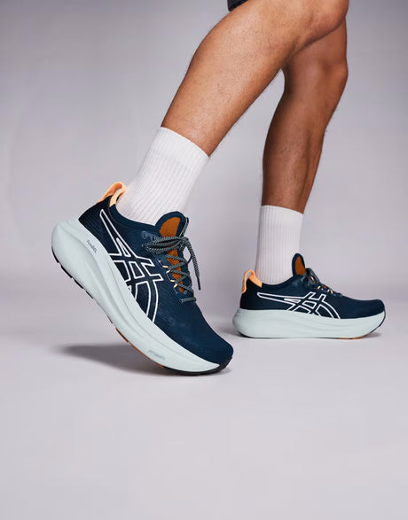 Navy running shoes with white soles worn by a person on a light gray background
